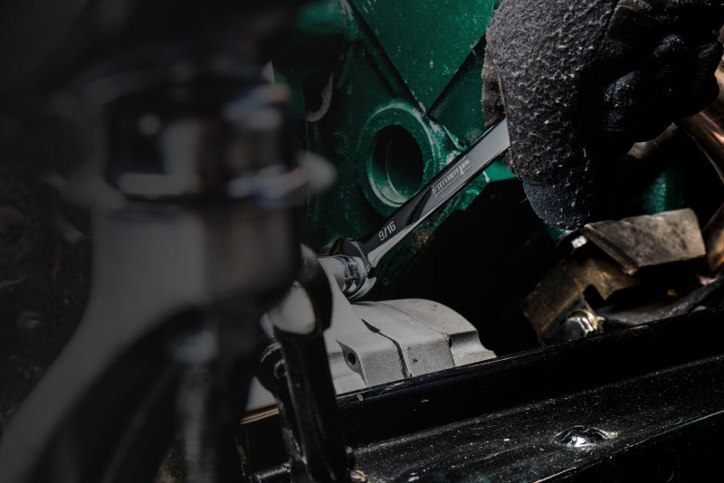 The hand of a mechanic wearing a work glove and holding a wrench. The wrench is being used to adjust a fastener in some machinery.