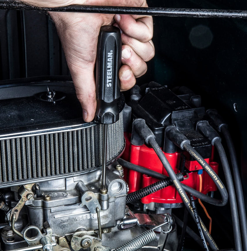 A mechanic uses a black STEELMAN screwdriver to tighten a screw in a vehicle’s engine compartment