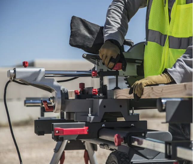 A worker uses a miter saw mounted on a STEELMAN portable workstation to cut lumber. 