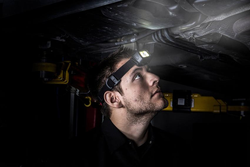 A mechanic wearing a STEELMAN headlamp examines the undercarriage of a vehicle that is sitting on a lift in an auto shop