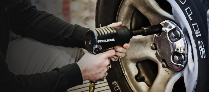 A mechanic using a STEELMAN pneumatic impact driver to remove lug nuts from a vehicle’s wheel